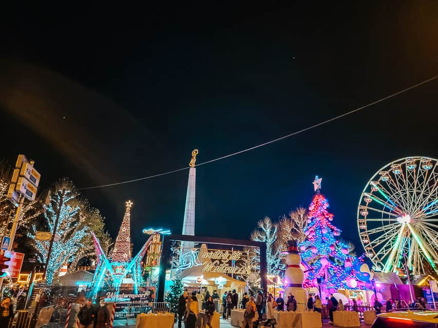 A view of the Place de la Constitution market - with lights, trees, and rides visible.