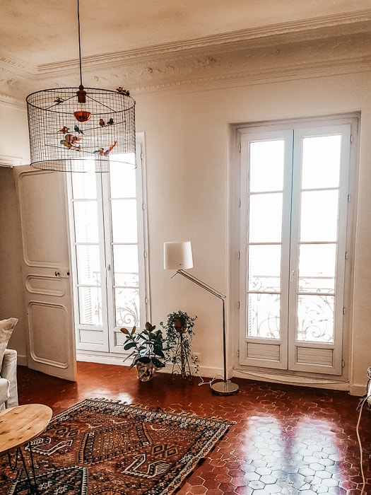 A traditional French apartment. Large windows light a tiled room with a large rug.