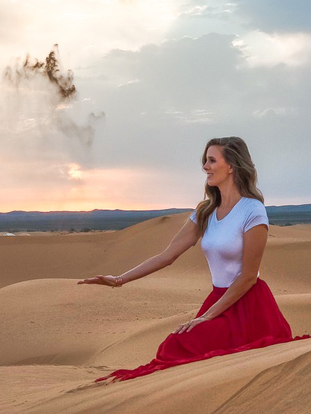 A woman in red and white kneeling in Moroccan sand dunes.