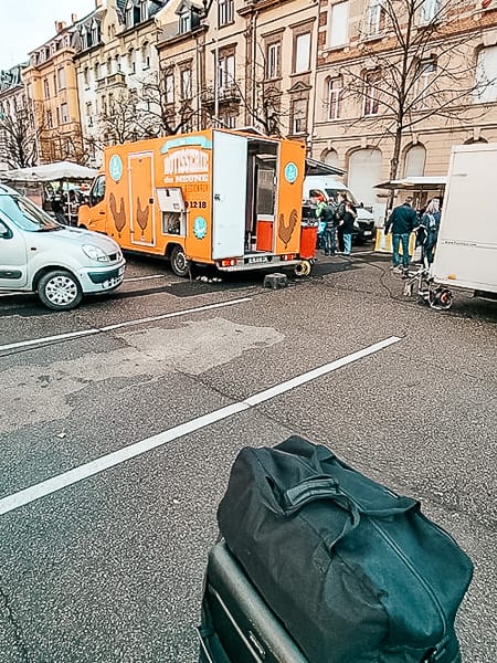 Luggage awaits a non-existent car. Food trucks in the background.