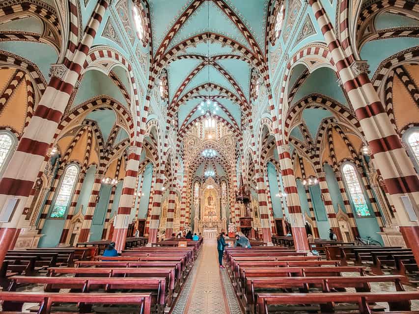 The interior of the candy cane church - arches with painted red and white stripes, blue ceilings, painted flowers, tiled floors, and dark wooden pews.