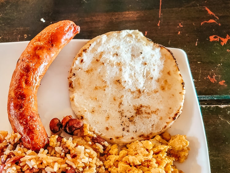 A Colombian breakfast plate with sausage, rice and beans, eggs, and arepa.