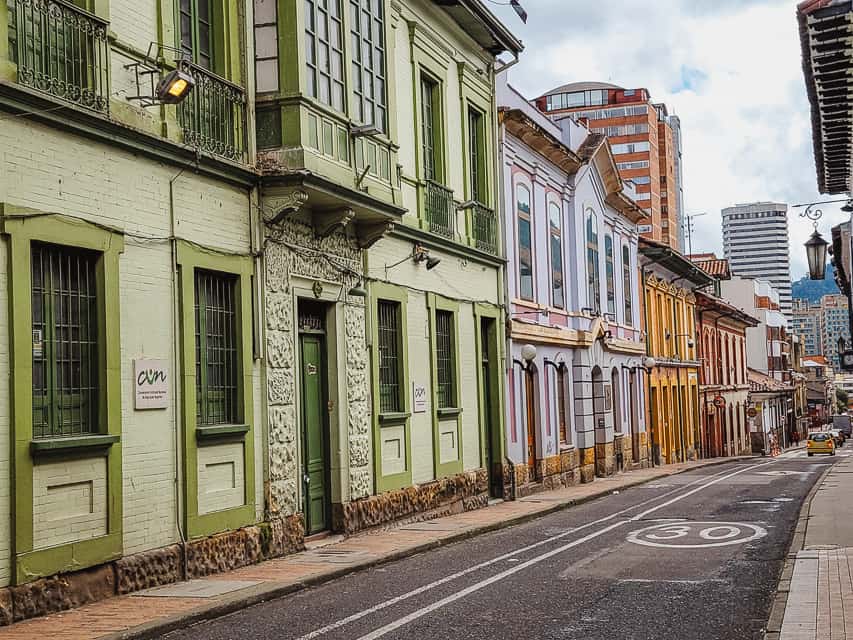 A street in Candelaria with green, purple, orange, and red buildings all in a row. Exploring Candelaria is one of the nicest things to do in Bogota with three days.