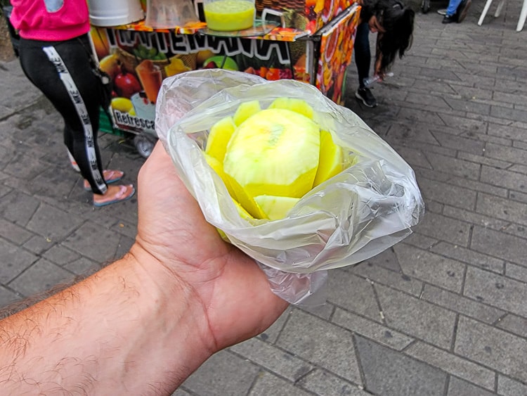 A sliced Mango biche near a fruit stand. A green, crunchy, tart fruit. They are green mangoes.