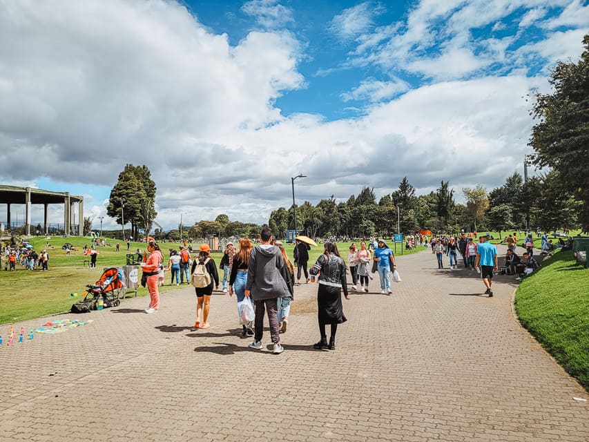 A wide walkway through the Parque de Simon Bolivar, with lots of greenspace on either side. Many people walk on the sidewalk or are lounging on the grass.