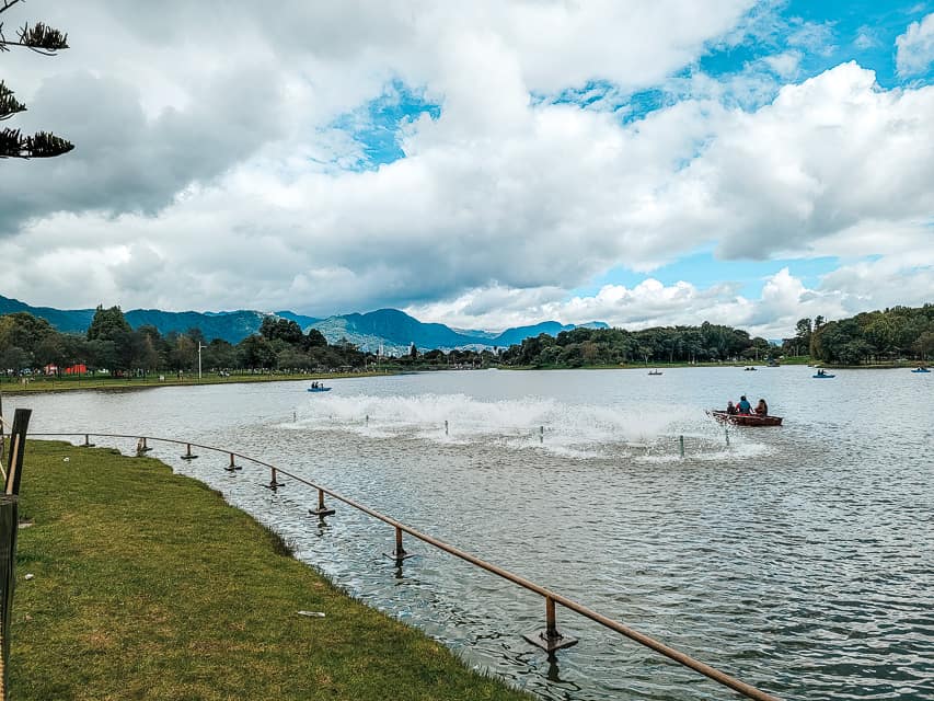 The lake in Simon Bolivar, its quite large, iwth several people on rowboats on the lake. Greenery and trees are lining the lake and some bigger hills/mountains are in the background. This park is one of the best things to do with 3 days in Bogota.