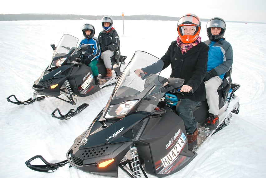 Two snowmobiles, with two people on each, sit on a frozen lake.