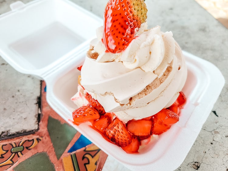 A dessert that is cream, strawberries, and a meringue sits in a white styrofoam box.