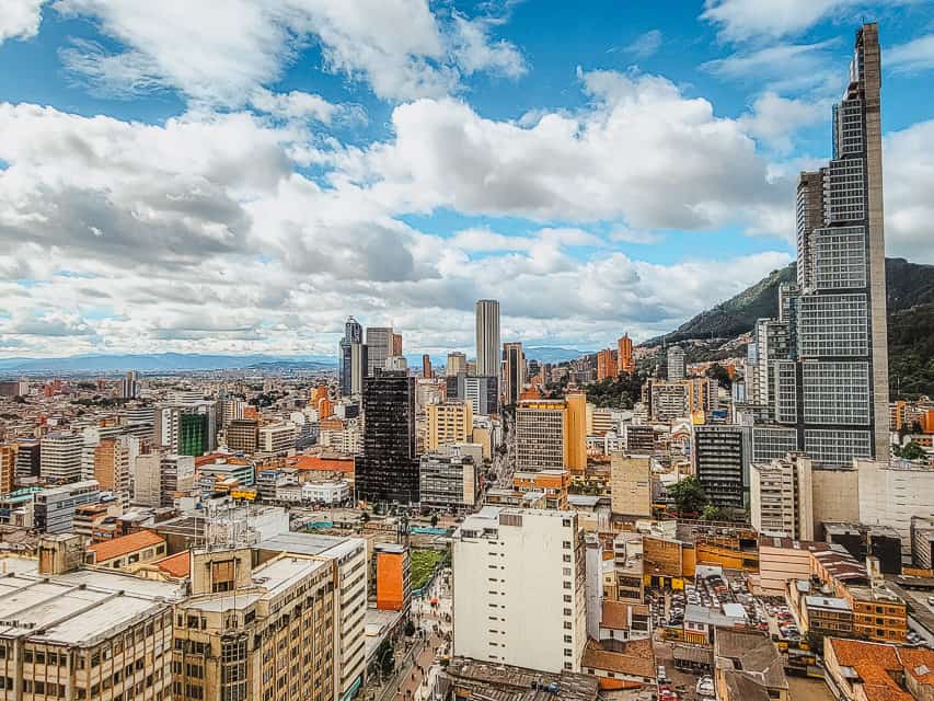 An aerial view over Bogota, with buildings and some skyscrapers visible, and a couple of hills in the background.