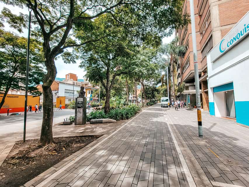 The street in Medellin with checkered sidewalks with trees lined up parrelell to the buildings