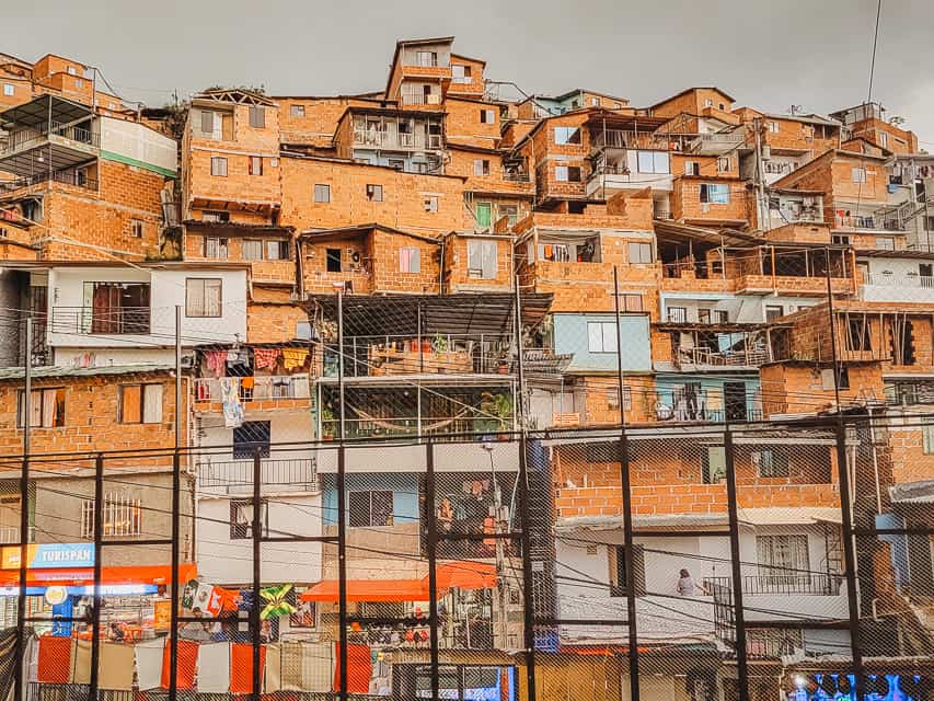 A very poor neighboorhood area with houses leading up the mountain and fences surrounding the neighborhood. The buildings are all brown brick colored and very small.