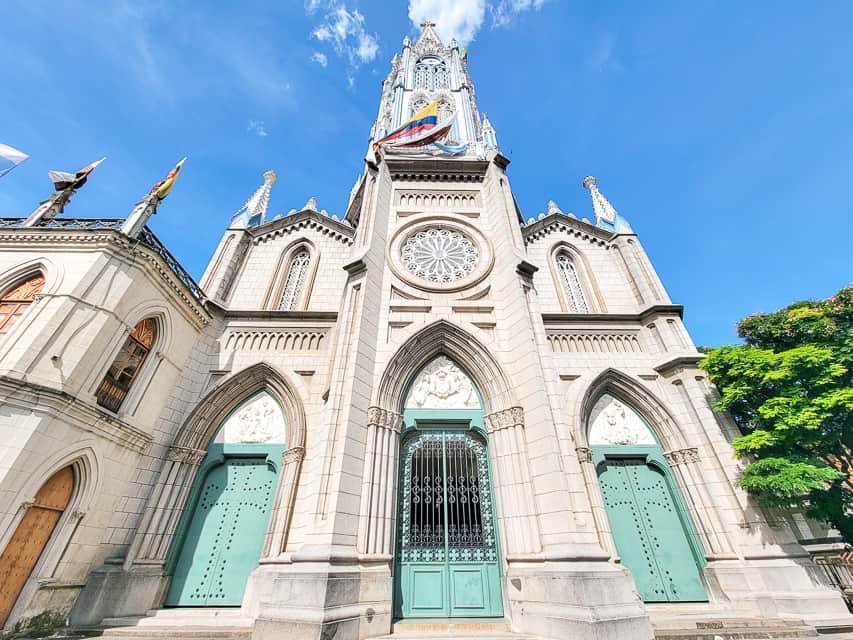 A white stone cathedral with a spire that is super tall and has many windows. There are many intricate engravings all around the gorgeous building