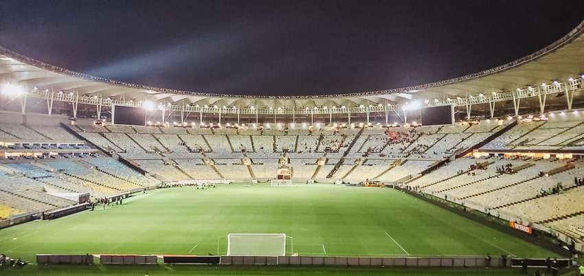 A football stadium with green grass and metal frames all around the top protecting the metal seats all around the arena.