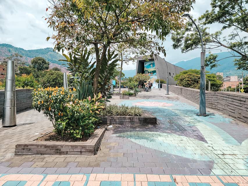 A park like exihbt with stone guardrails looking over the mountain sceney, Inside the overhand area there are lots of colorful flowers and trees.