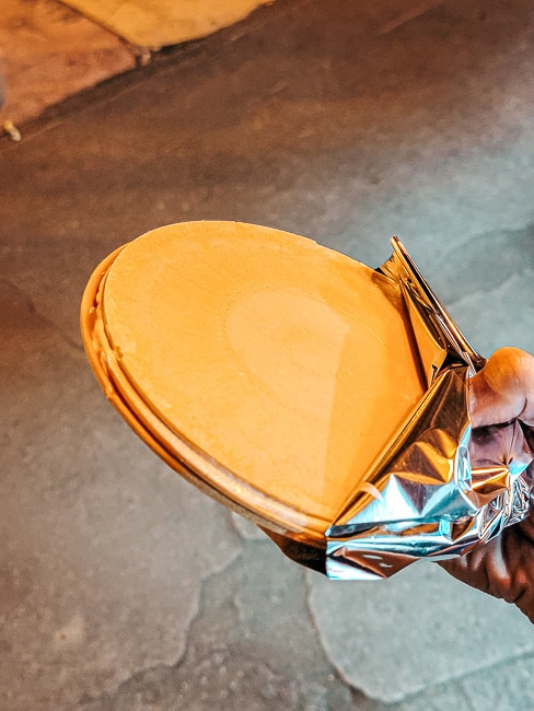 A hand is holding an obleas (two golden wafters with arequipe in the middle) in aluminum foil.
