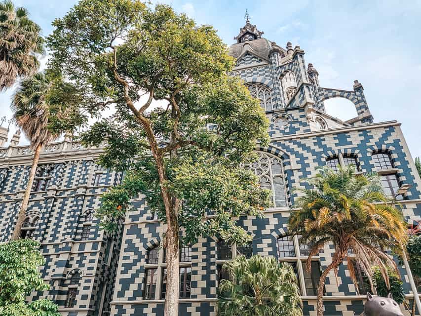 A white and blue mosaic checkerboard like cathedral with trees in front of the doors.