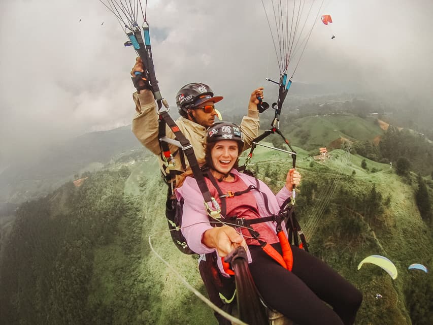 A woman paragliding over the mountains next to Medellin. There are very lush and green trees all around the area.
