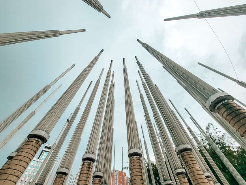 A square with around 300 skinny stone pillars that light up at night. The pillars are brown and tan-ish.