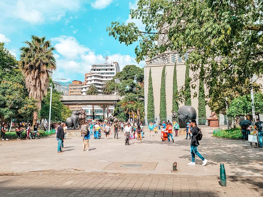 A square with cement and bricks. there are many buildings and statues assorted around and many assorted plants around.