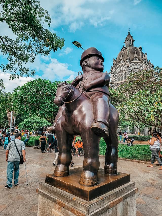 A bronze statue of a squat man with a bowler hat on a horse with a very small head.