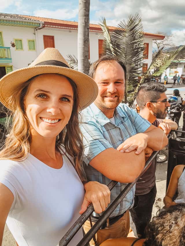 A smiling man and woman stand on the back of a jeep.
