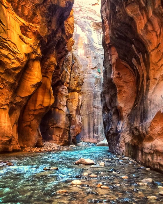 A breathtaking slot canyon with interlacing walls and a shimmery blue river with lots of rocks on the bottom.