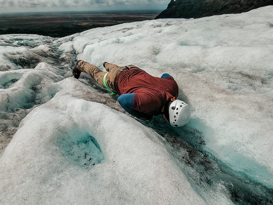 A man lays on the glacier to drink some deep blue glacier water on a glistening glacier.