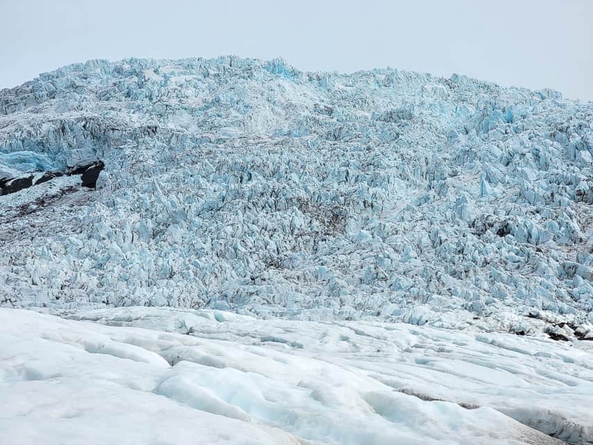 A blue snowy glacier with craggles carved into it stands in the skaftafell glacier