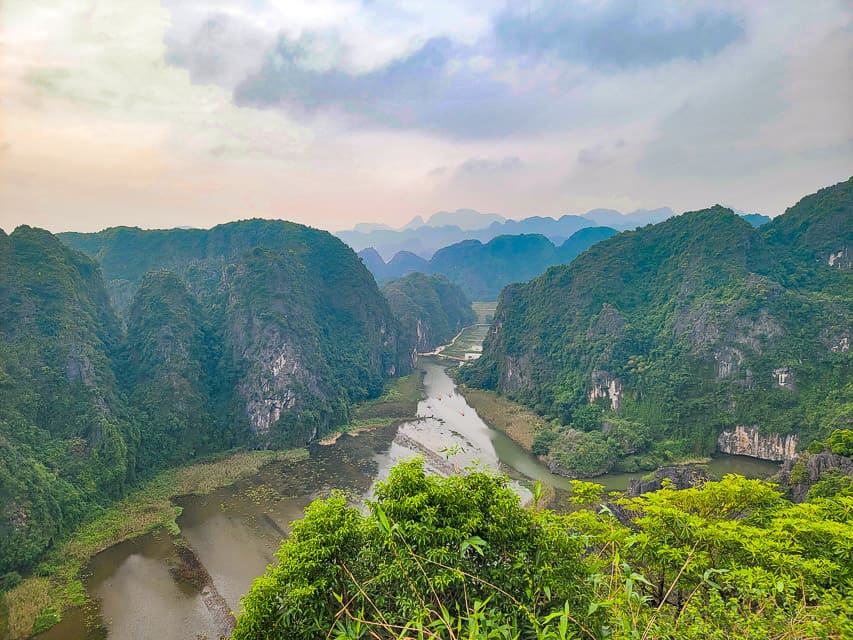 The view from the tip of the mountain. with multiple lush green rock mountains going far into the horizon with a small water channel curving through them.