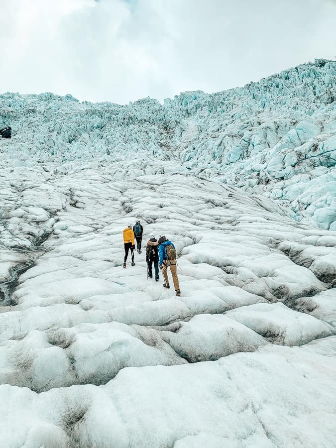 4 people hike the beautiful tall blue and white glacier.