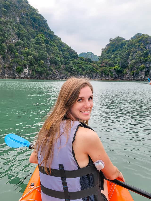 A woman with a gray lifejacket sits in a canoe looking at a large sheer rock formation.