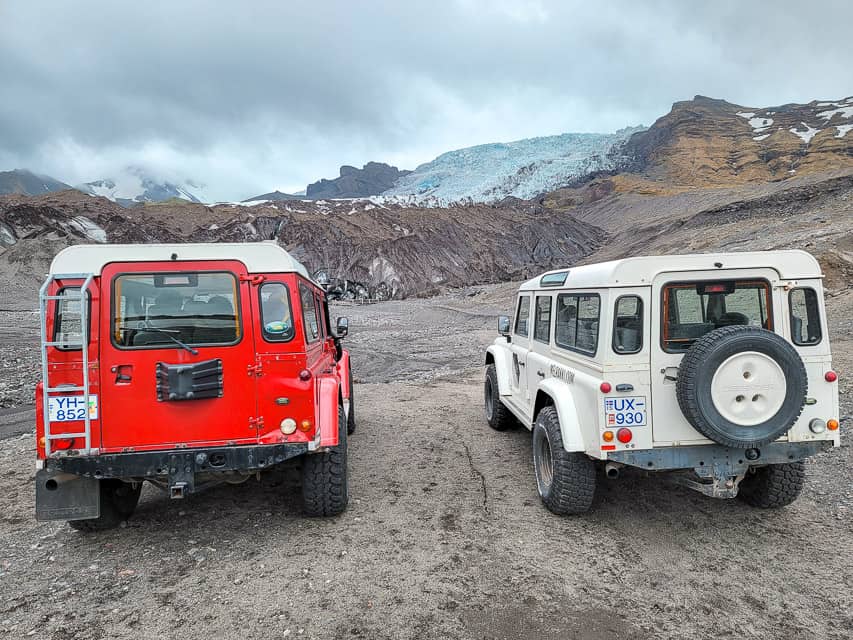 2 white and red jeeps park no the base of a dirt and rock hill that leads to the Skaftafell glacier.