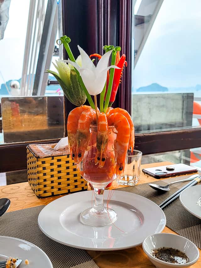 A specialty seafood dish with shrimp on a cup like dish and flowers and peppers on the side.