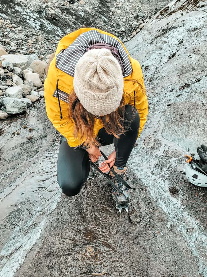 A woman in a yellow jacket put crampons (which are metal spikes) onto her shoes at the base of the watery glacier.