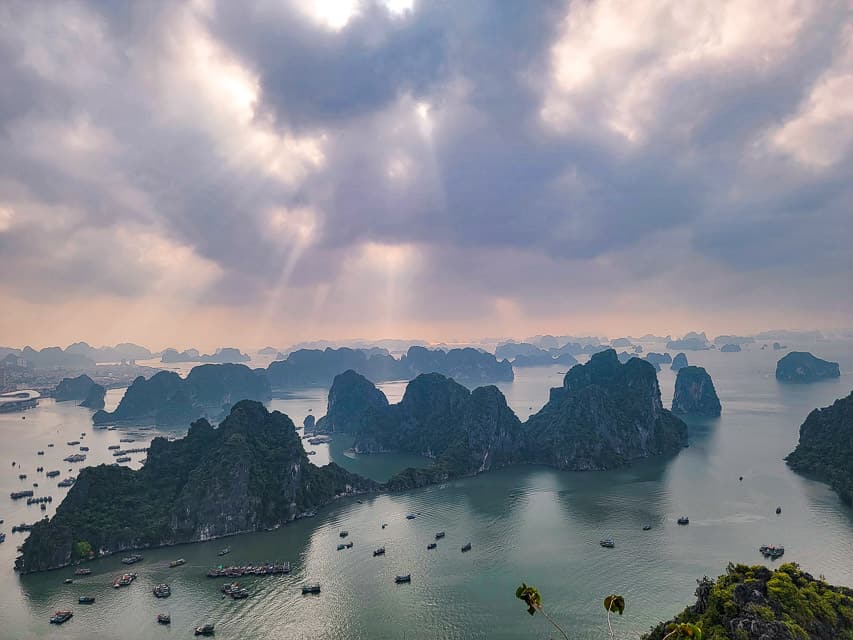 An aerial view of Halong By at the top of the large rocks with lots of boats cruising in the bay taking in the sheer rocks with the sunrise.