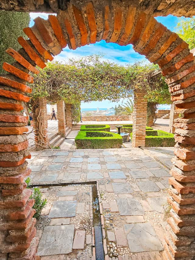 A look through a brick arch to a patio area with a trellis of greenery.