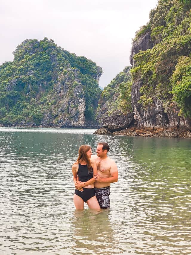 A man and woman hold hands on the shore of one of the floating islands with sheer cliffs and lots of green ferns on the sides.