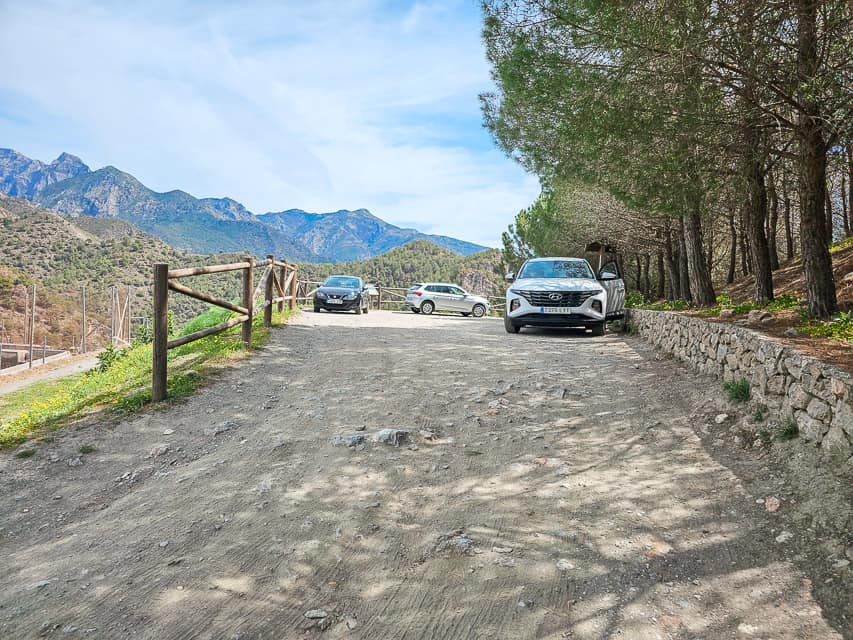 Multiple cars at the top of a viewpoint looking at the top mountain range.