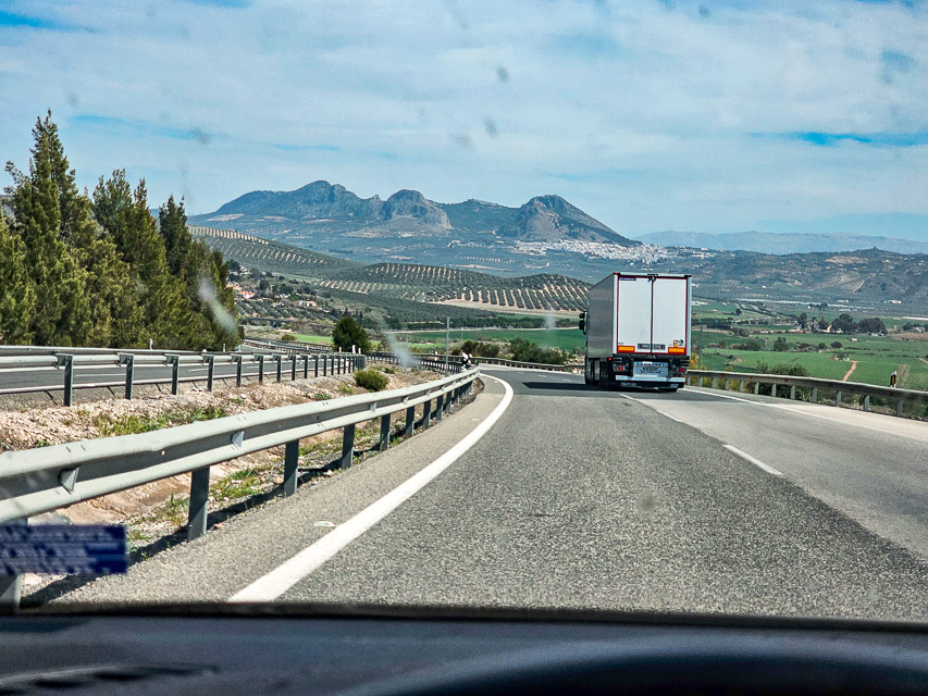 A view of the Spanish countryside from the highway. You can see olive groves and mountains in the background.