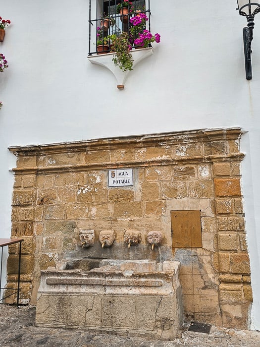 A tan, stone fountain featuring four stone faced spigots.
