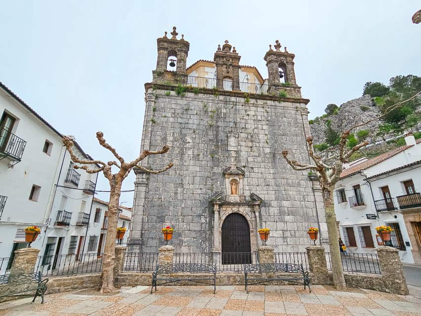 A stone church with three very small bell towers in town, with white buildings beside it.
