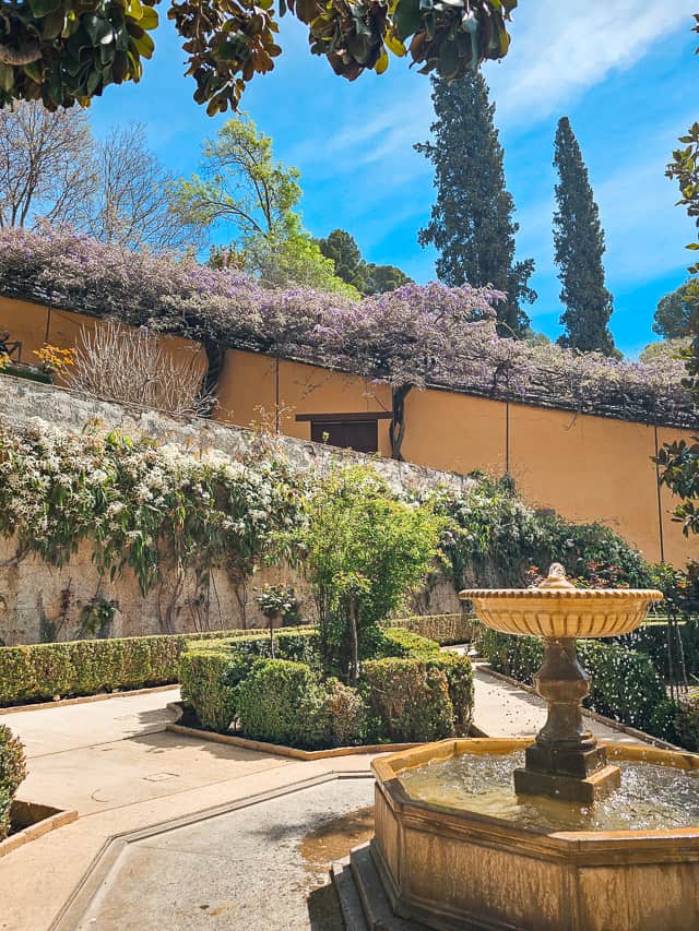 A small garden with a fountain, hedges, and wisteria in Generalife.