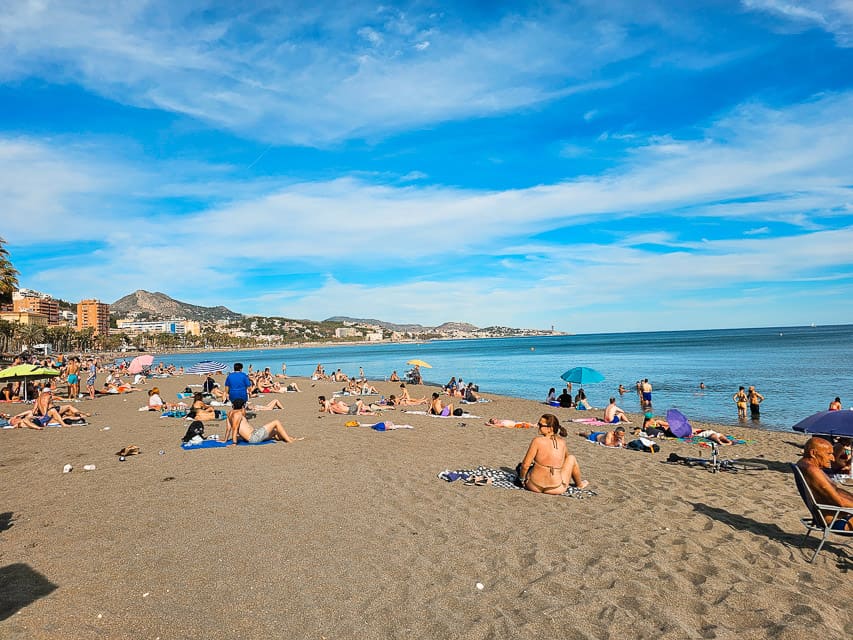Lots of people relax on the sand at Malaguetta Beach in Malaga, with the Mediterranean in the background.