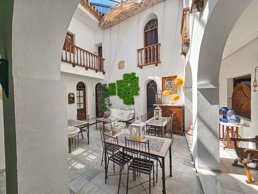 A very small courtyard with marble flooring, white arches, and a few tables and chairs are set up.