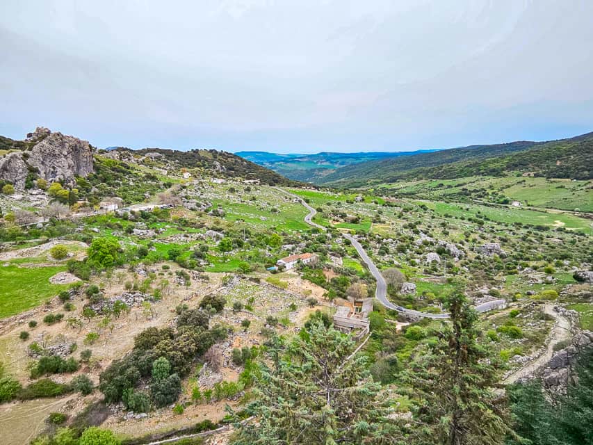 Looking over the valley in front of the town, with scrubby plants, green pasture, and a winding road going through it.