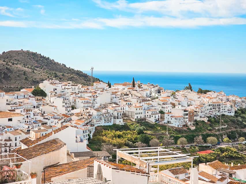 The view from the top of a hill looking down at the town of Frigilana with white buildings all around on the coast of the sea with the gorgeous colors shining in the sun.