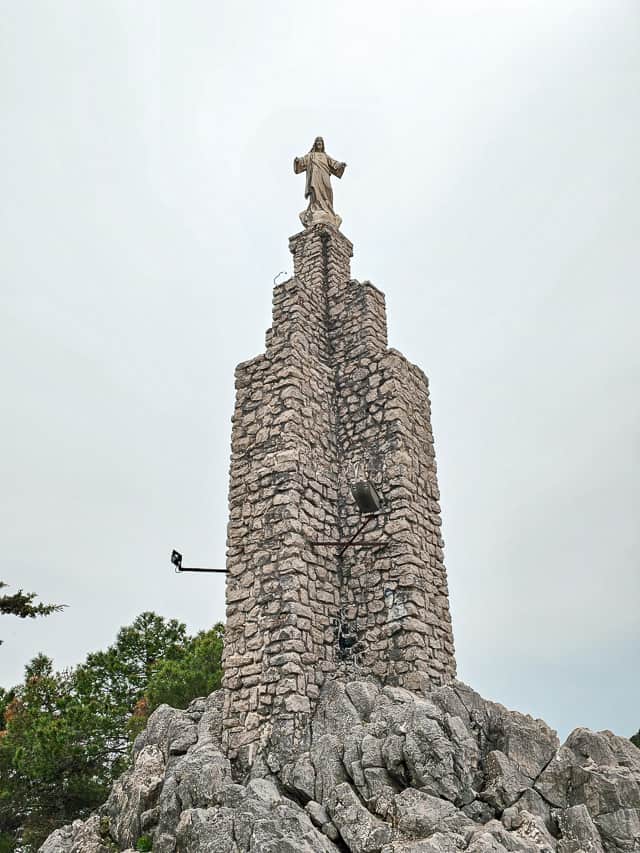 A stone pillar with a sculpture of Jesus on top of a hill near the town.