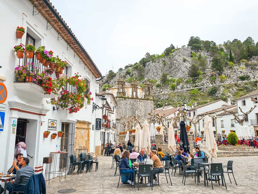 Another view of Plaza de Espana, with cobblestoned streets, white houses wiht flower pots on the balconies, and people sitting around tables at an outdoor restaurant.