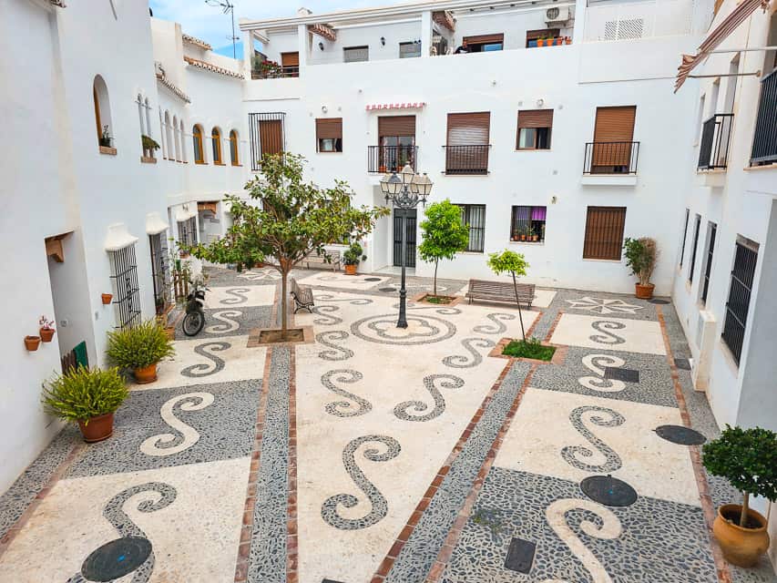 A cute small square with intricate black and white tilework tucked around white buildings