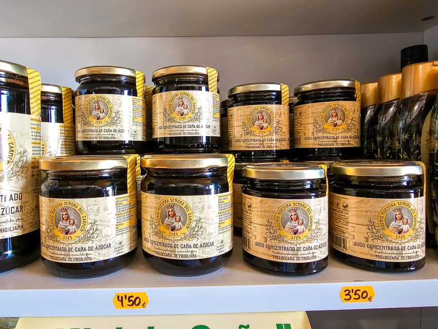 Rows of sugar cane honey and sugar in glass bottles on a white shelf.